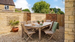 A patio with a table and chairs, surrounded by stone walls and a wooden fence. - Essitone: Cinema Room, Games Room, Gym & More! (Ashton Keynes)