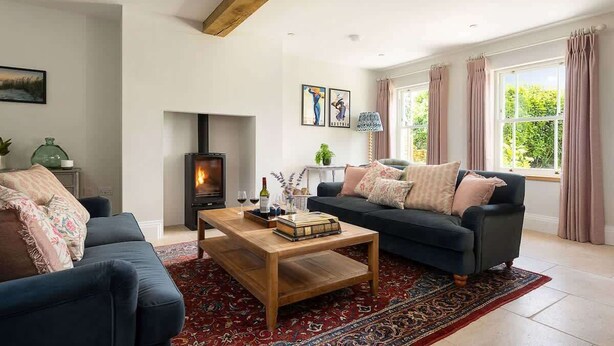 A living room with a fireplace, two sofas, a coffee table, and large windows with curtains. - Essitone: Cinema Room, Games Room, Gym & More! (Ashton Keynes)