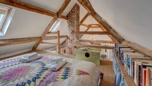 Um quarto de sótão acolhedor com teto de madeira, chaminé de tijolos, cama acolchoada e estante de livros.