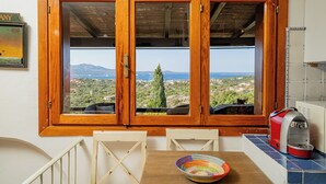 A room with a wooden-framed window overlooking a scenic landscape, a table with a colorful woven basket, and a red coffee maker on the counter.