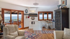 A spacious living area with a large window, a dining table, and a cozy seating arrangement.