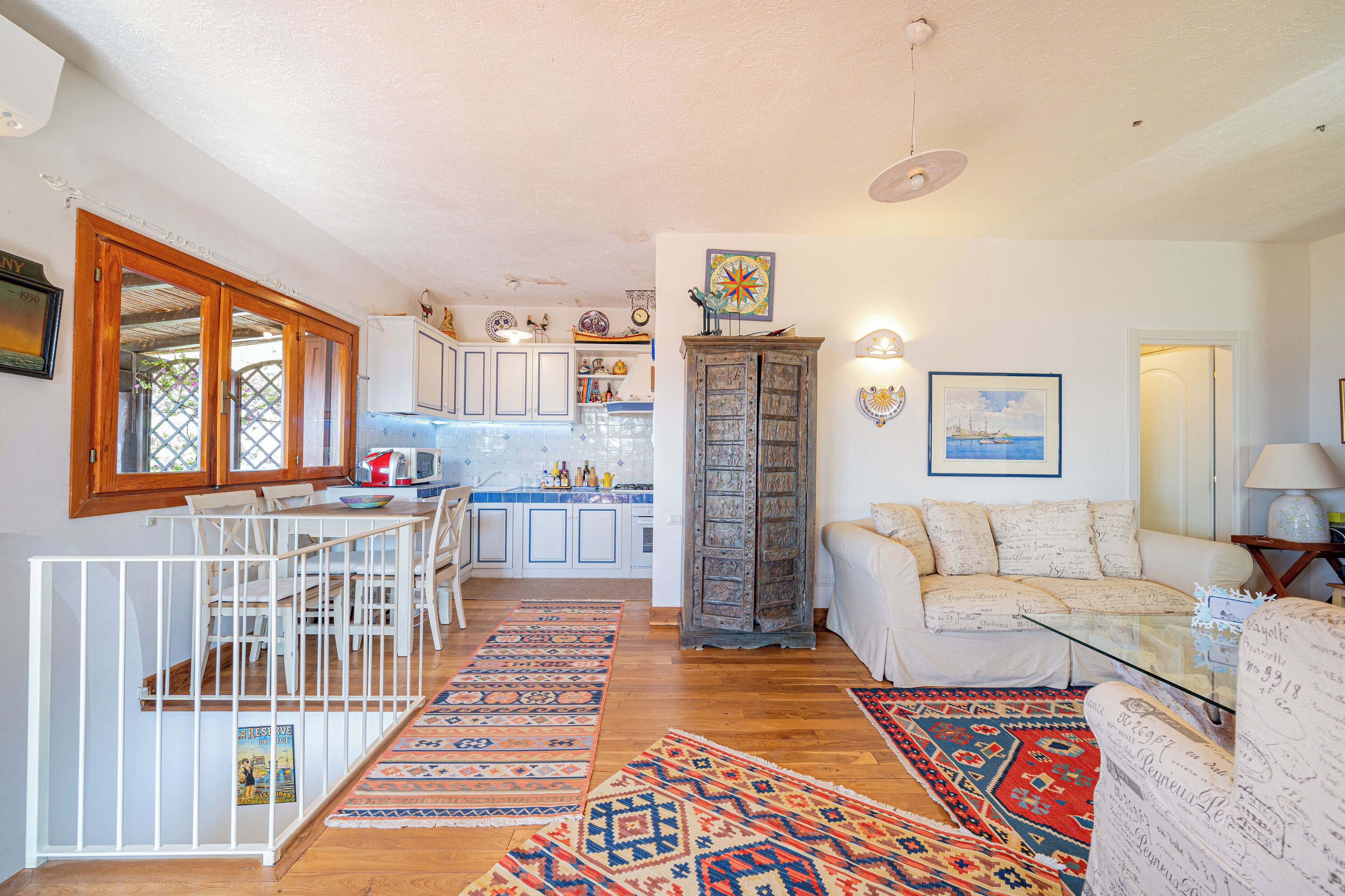A spacious living area with a sofa, a dining table with chairs, a kitchen in the background, and a staircase leading to an upper floor.