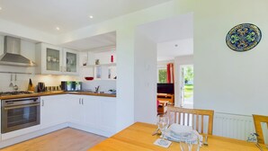 A modern kitchen with white cabinets, a stove, and a dining area with a table set for two. - Vermont Your Peaceful West Bay Retreat (Yarmouth)