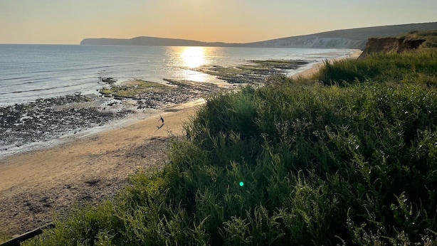 A coastal landscape with a beach, rocky shoreline, and vegetation. - Vermont Your Peaceful West Bay Retreat (Yarmouth)