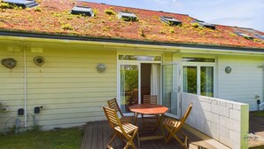 A yellow building with a green roof, a deck with wooden furniture, and a sliding glass door. - Vermont Your Peaceful West Bay Retreat (Yarmouth)