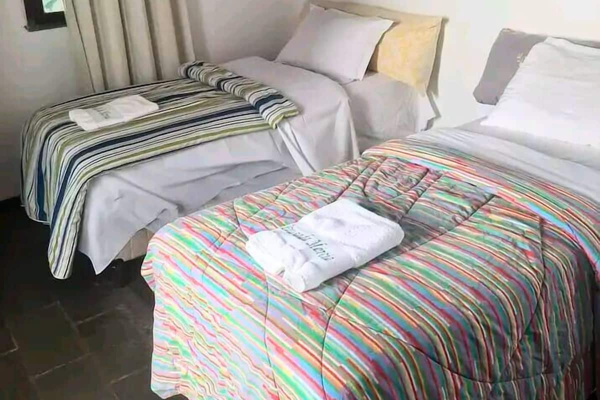 A bedroom with two beds, a window with curtains, a mirror, and a striped bedspread.