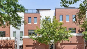 A modern building with a brick facade, multiple windows, and a tree in the foreground. - Charming Townhome in Omaha’s Historic Old Market  (Omaha)