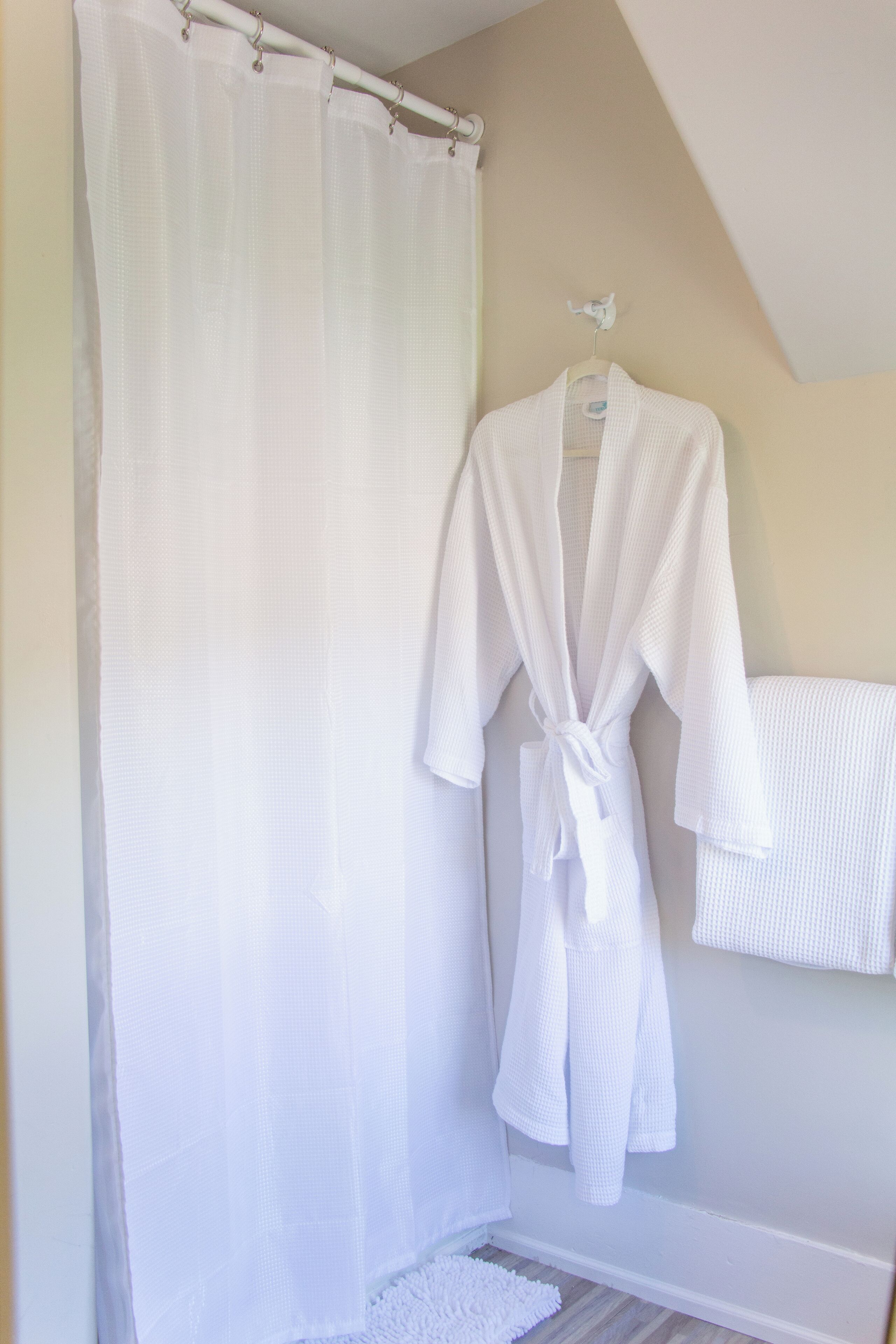 Een badkamer met een douchegordijn, een witte badjas hangend op een rek en een witte handdoek aan de muur.
