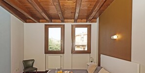 A bedroom with a bed, a chair, a tray with breakfast, and two windows. - Garofano P1-9 by Wonderful Italy (Desenzano del Garda)