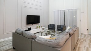 A modern living room with a sectional sofa, a flat-screen TV, and a glass coffee table.