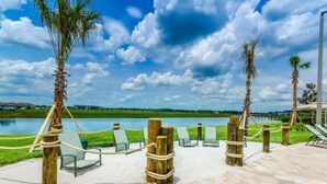 A waterfront patio with lounge chairs, palm trees, and a view of a lake.