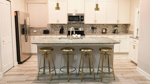 A modern kitchen with white cabinets, a granite countertop, stainless steel appliances, and gold bar stools.