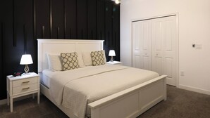 A bedroom with a white bed, two bedside tables with lamps, a black accent wall, and a white door.