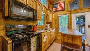 A wooden cabin kitchen with a stove, microwave, and wooden cabinets. - Grin & Bear It: brand new tiny home 1 bdr + loft w/ hot tub (Broken Bow)