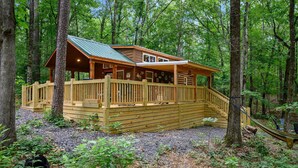 A wooden cabin with a porch and a staircase, surrounded by trees. - Grin & Bear It: brand new tiny home 1 bdr + loft w/ hot tub (Broken Bow)