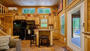A wooden cabin kitchen with a central island, a refrigerator, and a dining area with a couch. - Grin & Bear It: brand new tiny home 1 bdr + loft w/ hot tub (Broken Bow)