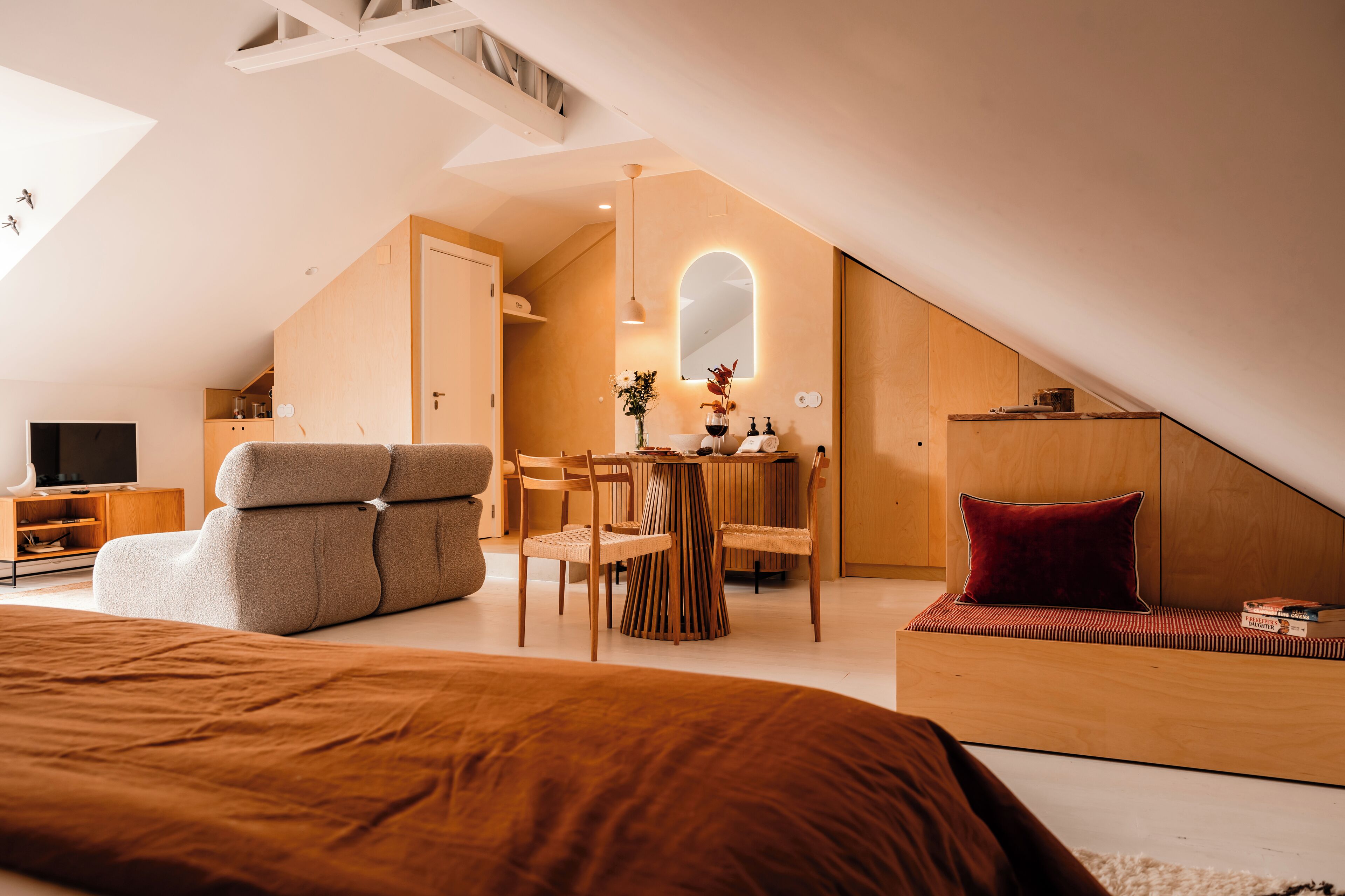 A modern bedroom with a sloped ceiling, a large bed, a seating area with a table, and a TV.