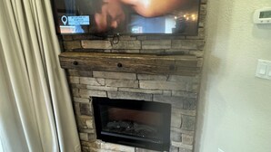 A living room with a stone fireplace, a flat-screen TV mounted above it, and a curtain on the left. - Cozy cabin with 2 bedrooms and WiFi, AC in soothing River Ranch (River ranch)
