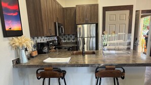 A kitchen with dark wooden cabinets, stainless steel appliances, a marble countertop, and two bar stools. - Cozy cabin with 2 bedrooms and WiFi, AC in soothing River Ranch (River ranch)