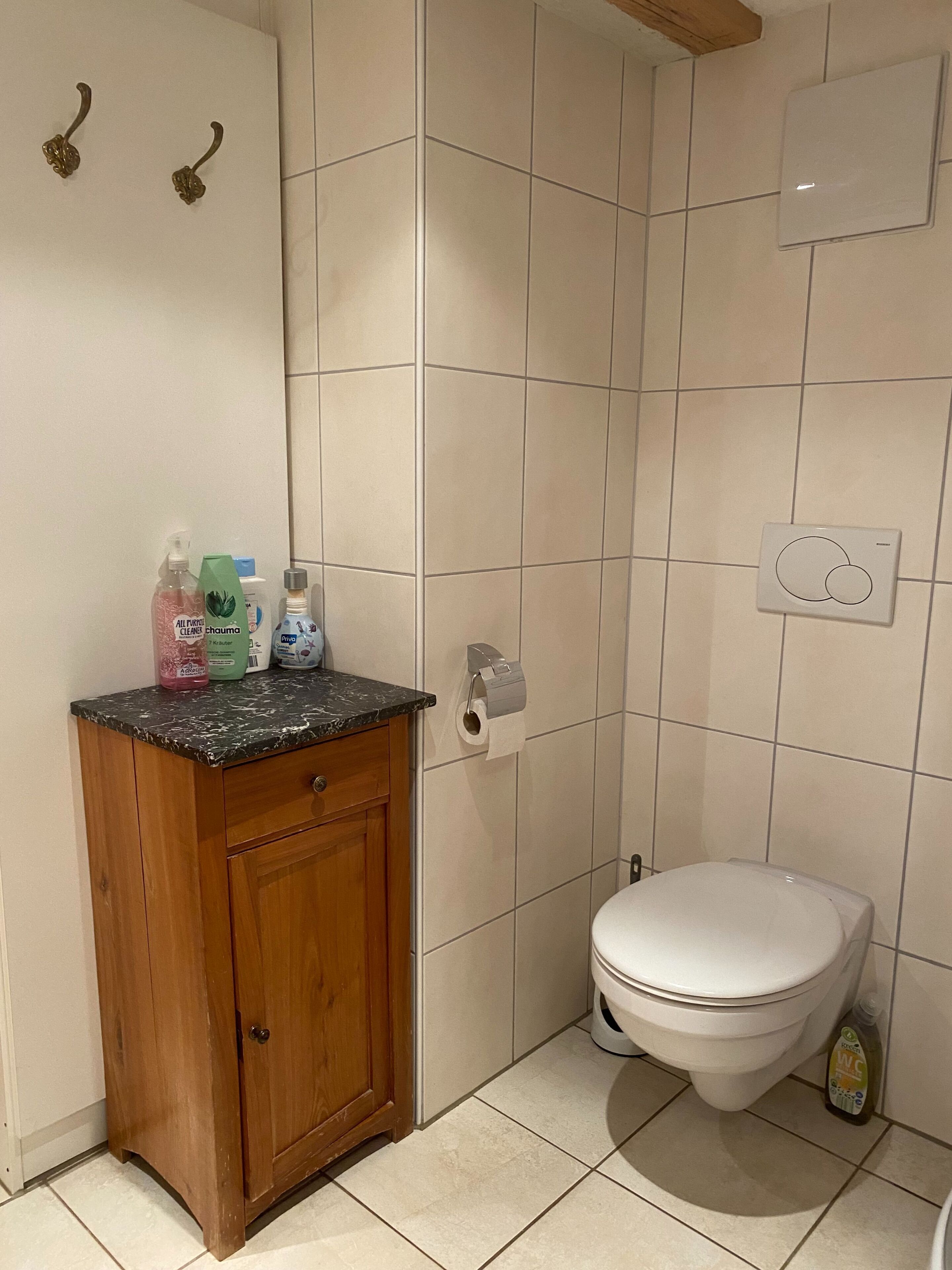 A bathroom with a toilet, a wooden cabinet, and a marble countertop with toiletries.