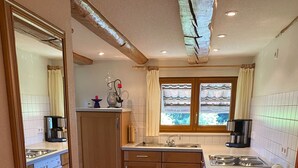 A compact kitchen with wooden cabinets, a built-in oven, a sink, and a window with curtains. - Holiday Apartment Cherry Blossom (Schuttertal)