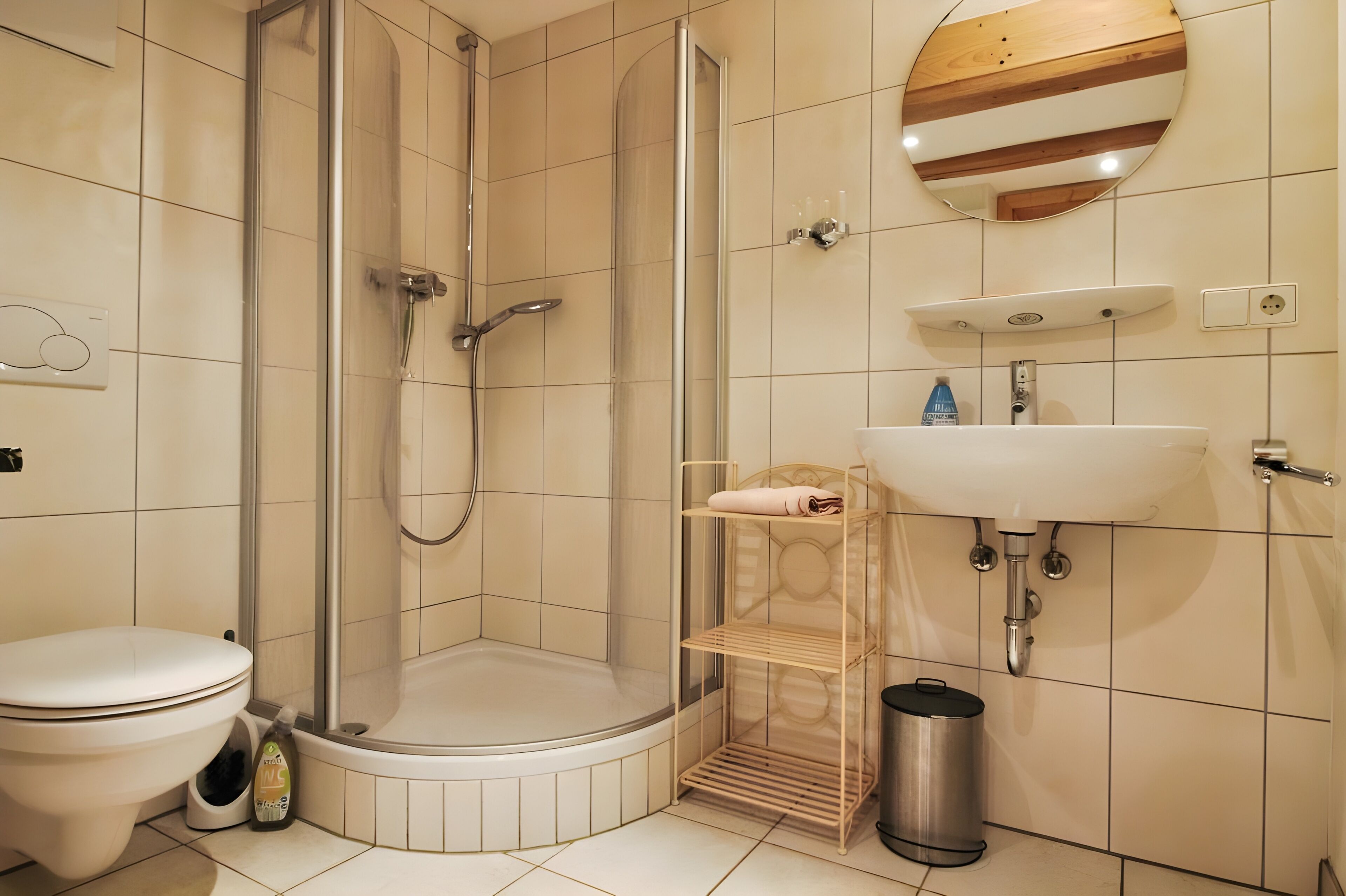 Ein modernes Badezimmer mit einer gläsernen Duschkabine, Toilette, Waschbecken und Mülleimer.