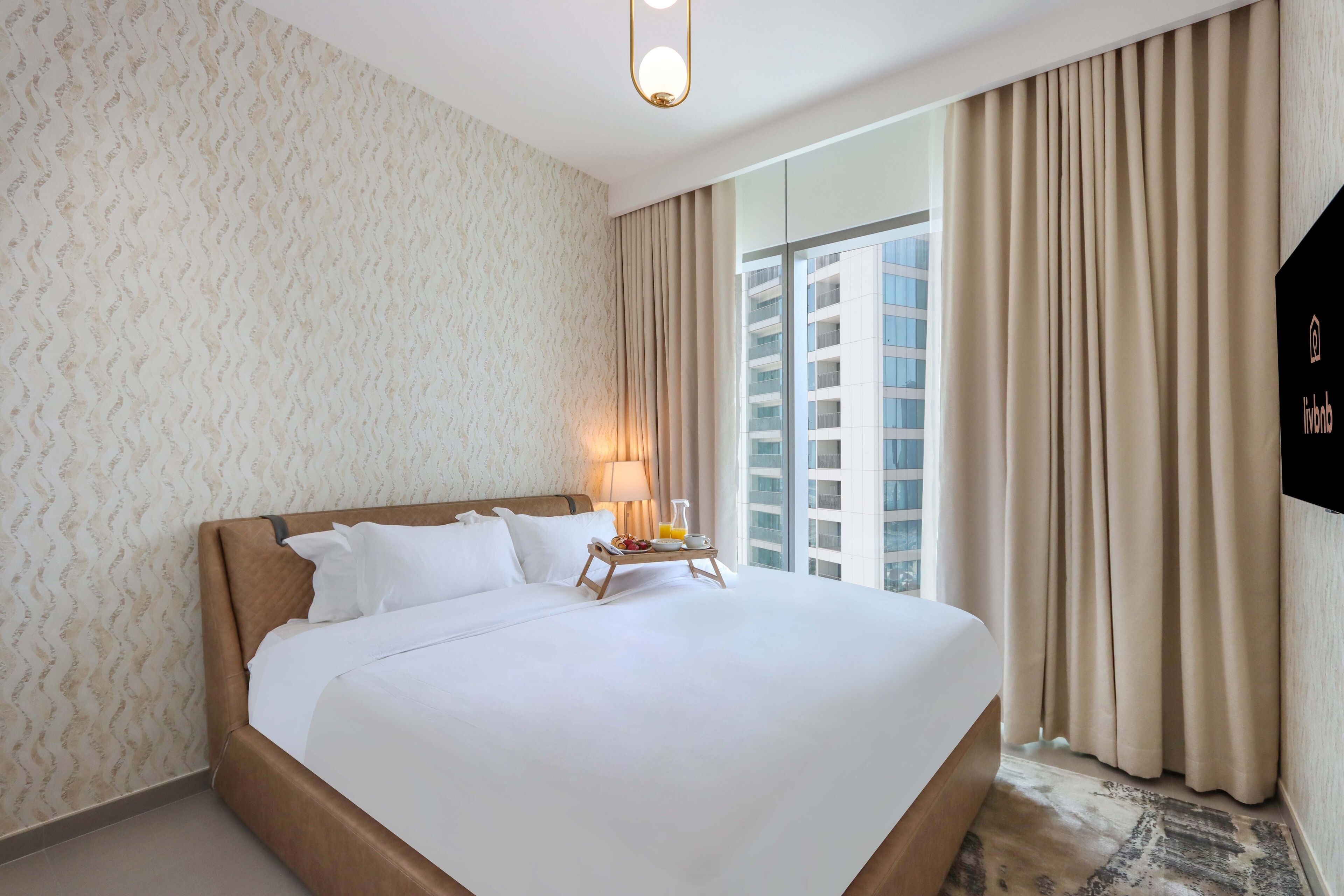 A hotel room with a large bed, a bedside table with a lamp, and a view of a building through the window.