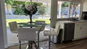Cocina moderna con comedor, que incluye una mesa de vidrio, sillas blancas y un lavamanos de acero inoxidable.