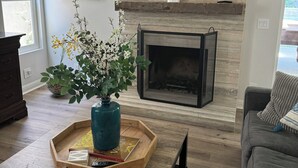 Una sala de estar moderna con chimenea, una mesa de centro con libros y un jarrón, y un sofá gris.
