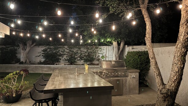 Un patio al aire libre con barra, taburetes, una parrilla y luces colgantes.