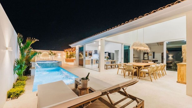 A modern outdoor pool area with a dining setup and a bar. - Luxury Residence Palm Beach | Villa Amandari (Noord)