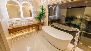 A modern bathroom with a freestanding bathtub, a large mirror, and a stone wall. - Luxury Residence Palm Beach | Villa Amandari (Noord)