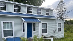 A two-story house with a blue door and windows, surrounded by a garden with rocks and plants.