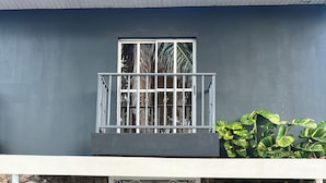 A hotel entrance with a stone wall, a balcony with metal railings, and a person standing at the door.