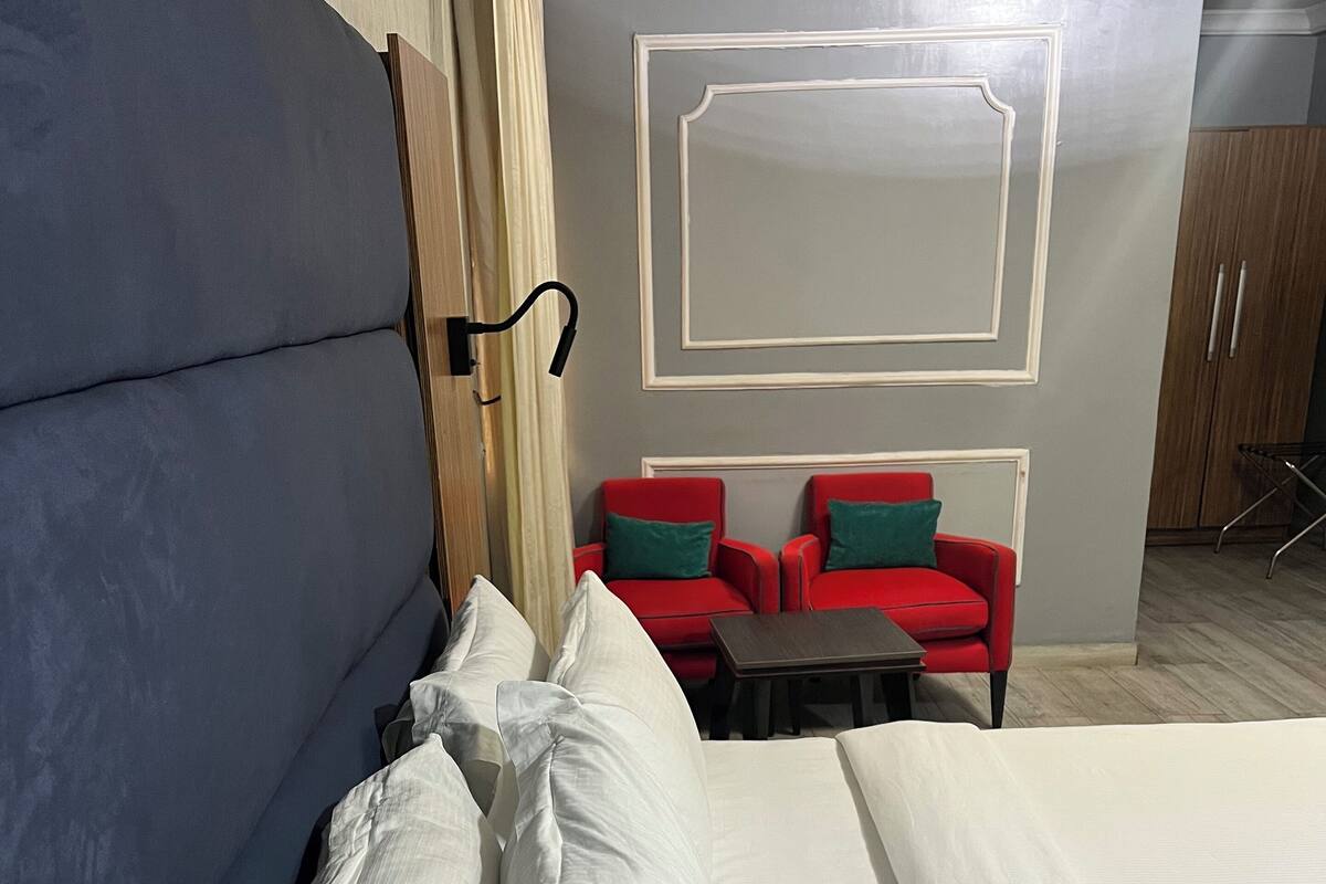 Une chambre d’hôtel avec un grand lit, une petite table et deux fauteuils rouges dotés de coussins verts.