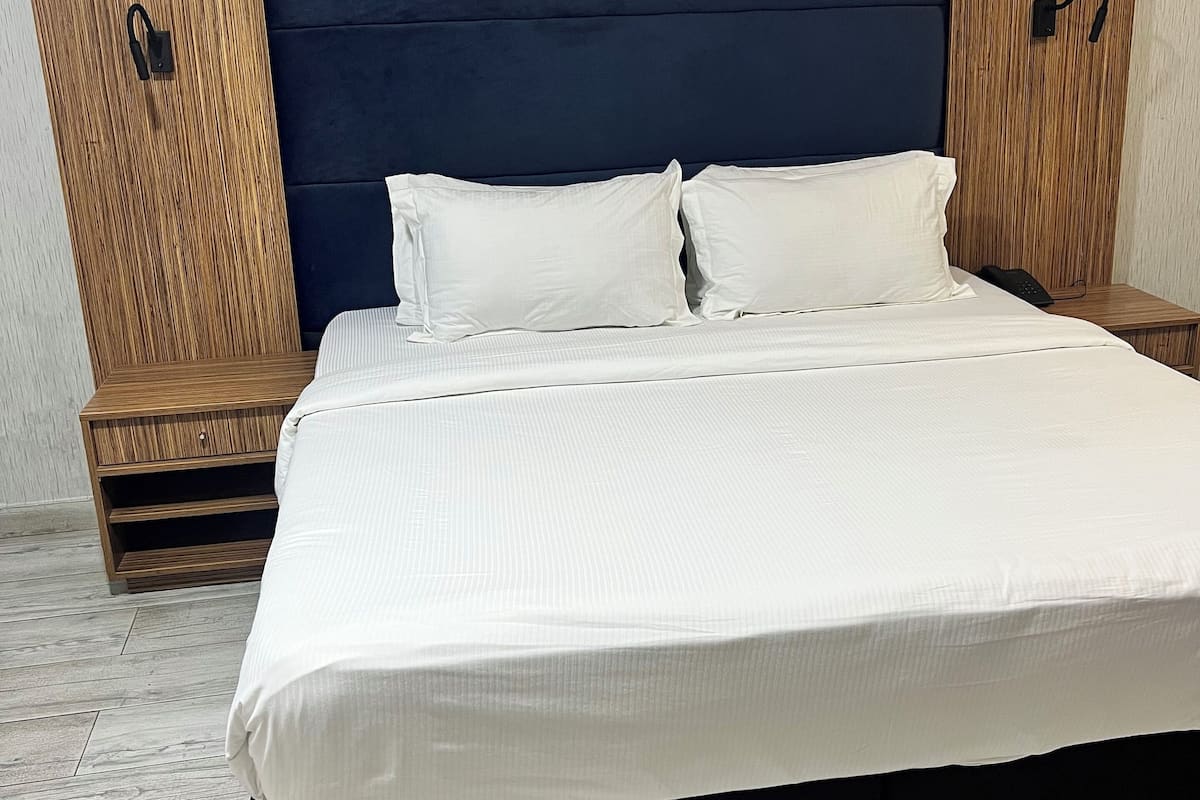 Une chambre à coucher moderne avec un grand lit, une tête de lit sombre, des tables de chevet en bois et un plancher de couleur claire.