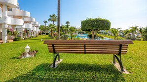 A bench in a well-maintained garden with a pool and palm trees in the background. - M11 Antares - Apartment (Sitio de Calahonda)