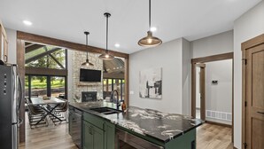 Una cocina moderna con una isla grande, luces colgantes y una chimenea de piedra.