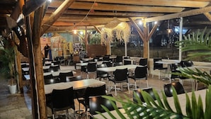 Ein Restaurant im Freien mit Holztischen und -stühlen, einem Backsteinboden und hängenden Pflanzen.