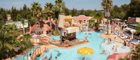 A large outdoor swimming pool with multiple water features, palm trees, and a variety of seating areas.