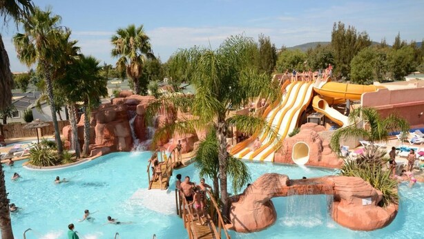 Ein Wasserpark mit großem Schwimmbecken, Wasserrutschen und Felsformationen.