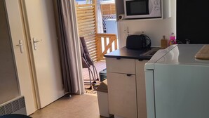 Eine kompakte Küche mit Mikrowelle, kleinem Kühlschrank und Spüle. Ein Holzboden ist durch eine geöffnete Tür sichtbar.