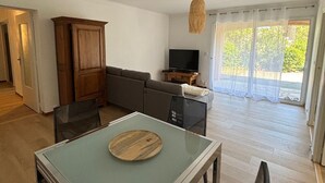 A dining area with a table and chairs, a sofa, a television, and a view of the outdoors through a glass door. - Appartement 70m2 Climatisé à Saint Aygulf (frejus)