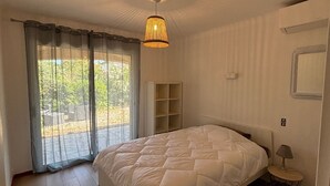 A bedroom with a large bed, a bedside table, a lamp, a wardrobe, and a window with curtains. - Appartement 70m2 Climatisé à Saint Aygulf (frejus)