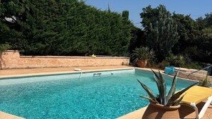 A clear swimming pool with a tiled edge, surrounded by a stone wall and lush greenery. - Appartement 70m2 Climatisé à Saint Aygulf (frejus)