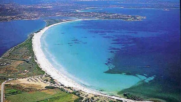 An aerial view of a coastal area with a curved beach, clear blue waters, and a distant island. - Gian s Home by Wonderful Italy (San Teodoro)