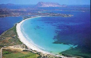 An aerial view of a coastal area with a curved beach, clear blue waters, and a distant island. - Gian s Home by Wonderful Italy (San Teodoro)
