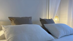 Una cama con ropa blanca y dos almohadas, una gris y otra blanca.