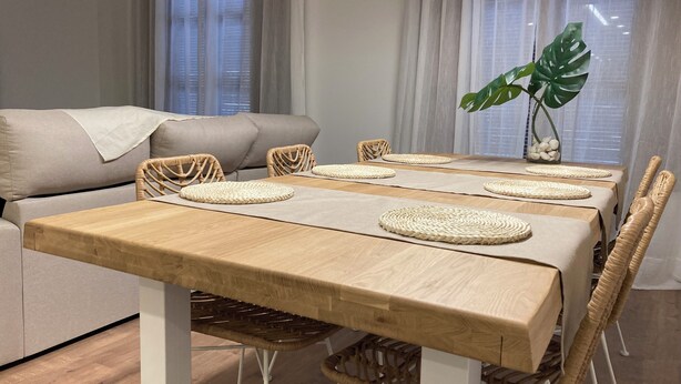 Un comedor con una mesa de madera, individuales tejidos, sillas de mimbre y un sofá al fondo.