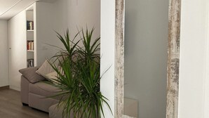 Een moderne woonkamer met een grote spiegel, een bank, een boekenplank en een potplant.